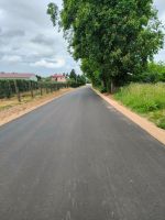 Droga asfaltowa w miejscowości Nowe Szwejki. W oddali po lewej stronie widoczny budynek mieszkalny, po prawej stronie...